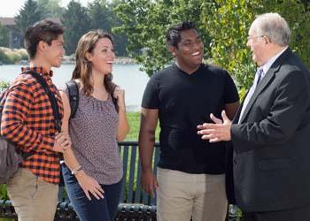 A professor and 3 students talk outside by a lake